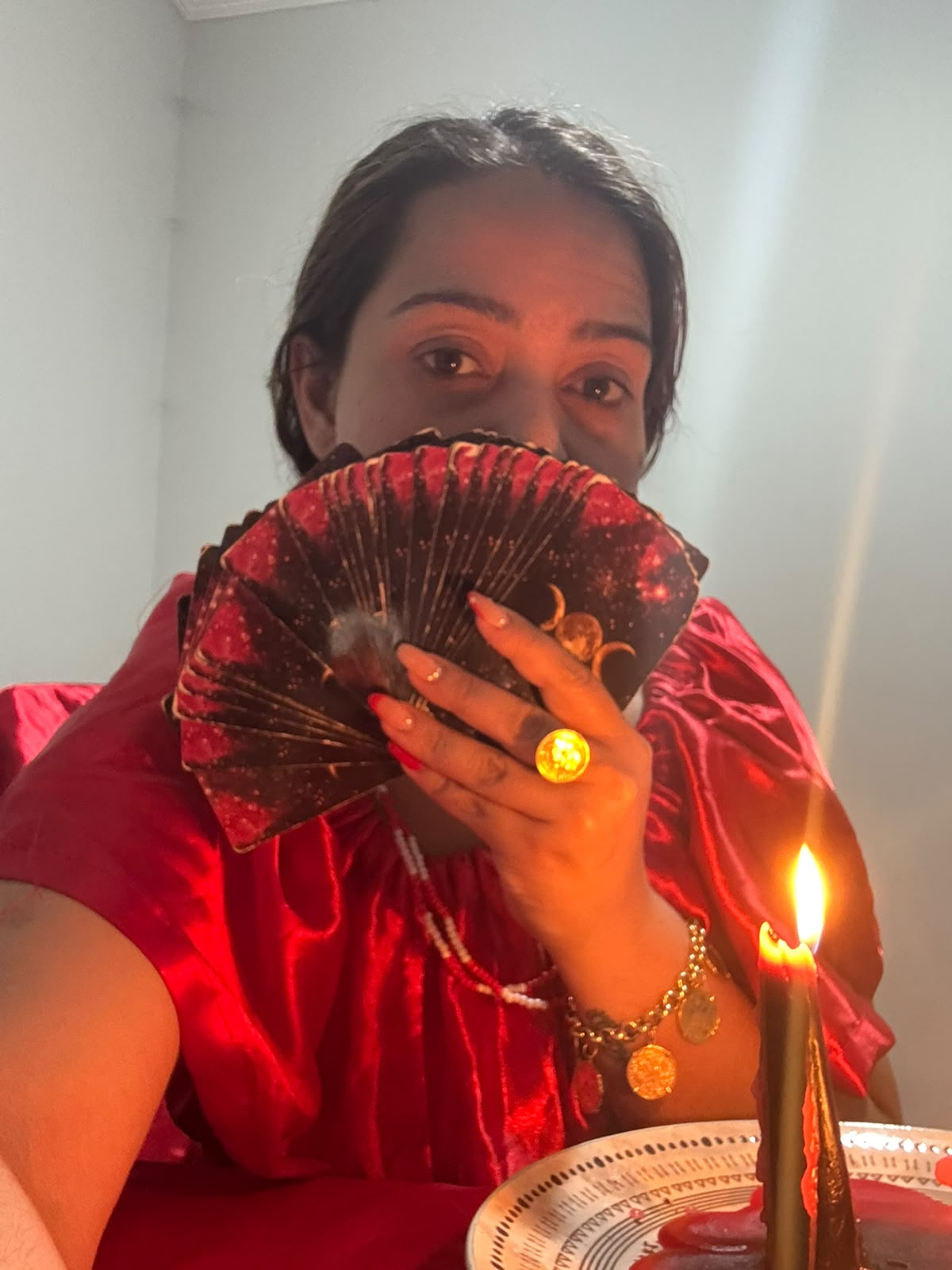 Taróloga Natália com leque de cartas à frente do rosto, à luz de vela